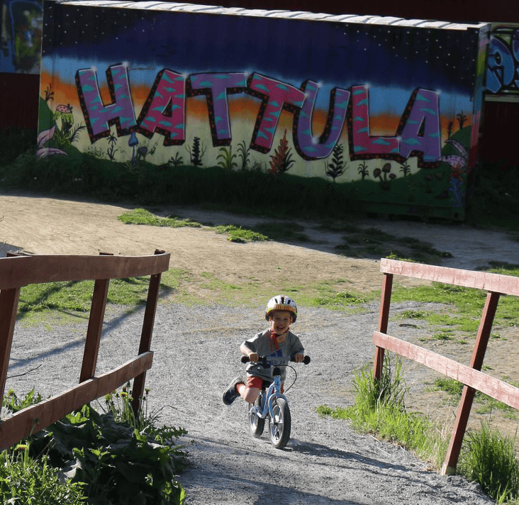 Taustalla Hattula-graffiti ja naurava lapsi potkupyörällä.