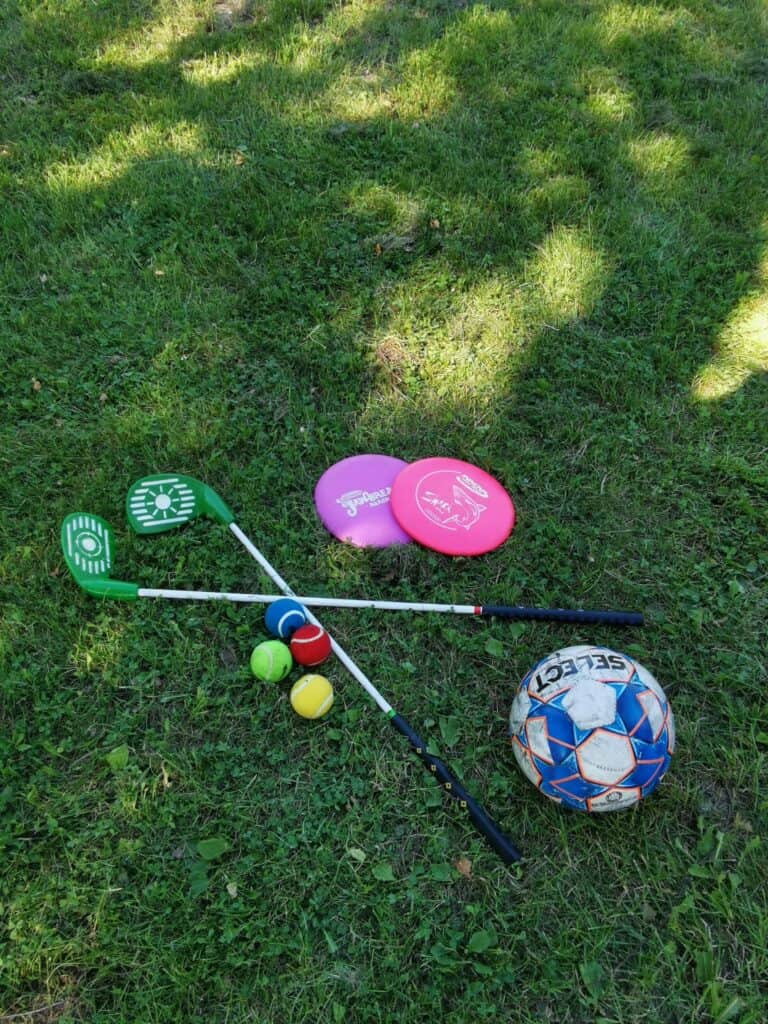 Mailoja, erilaisia palloja ja frisbeitä nurmikolla.