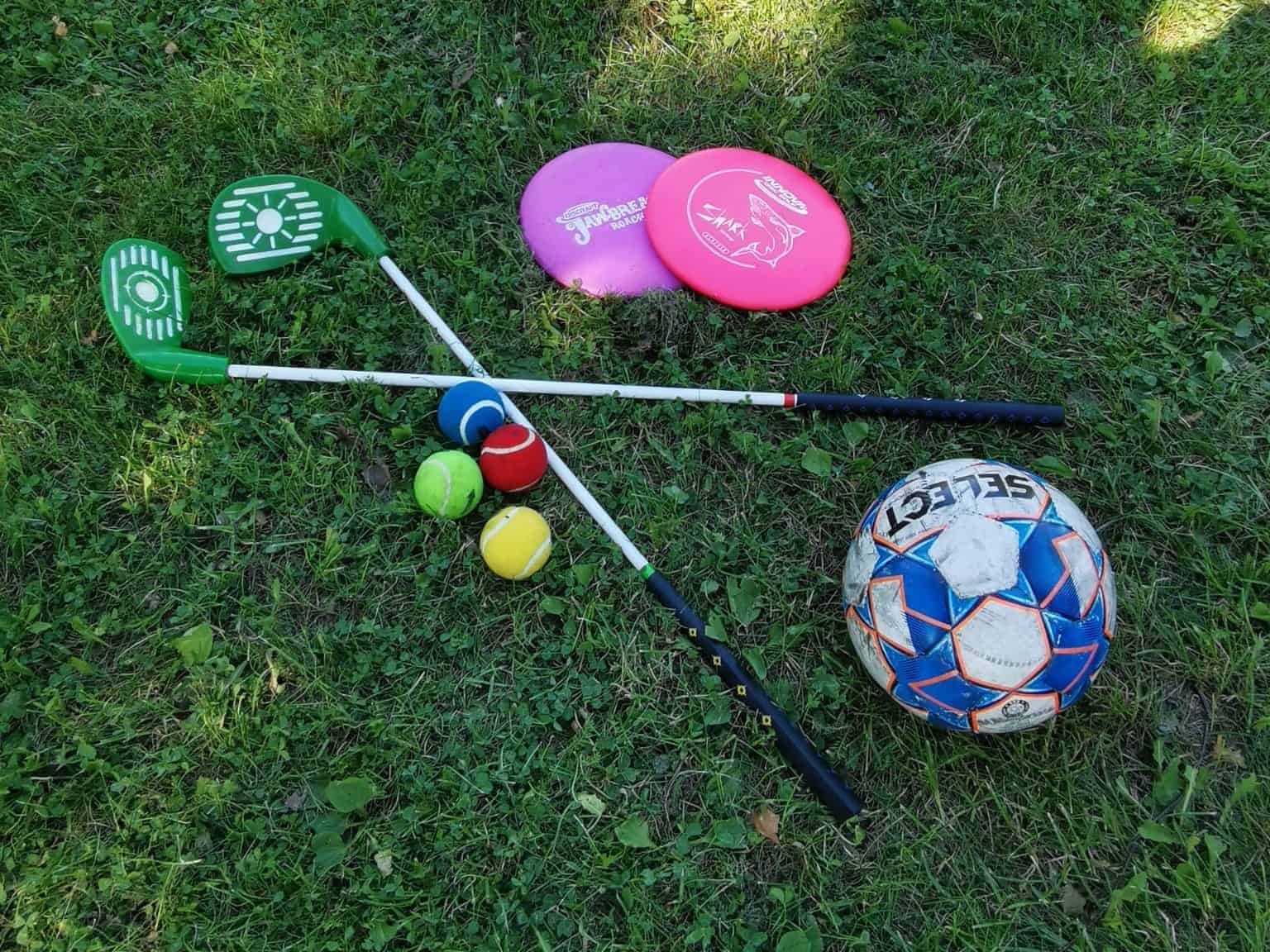 Mailoja, erilaisia palloja ja frisbeitä nurmikolla.
